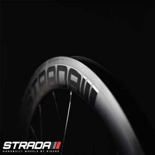 A close up of aStrada PAR Carbon 55 Ultra Performance Aero rim brake bicycle wheel rim in Black displaying the Strada logo with black picture background.